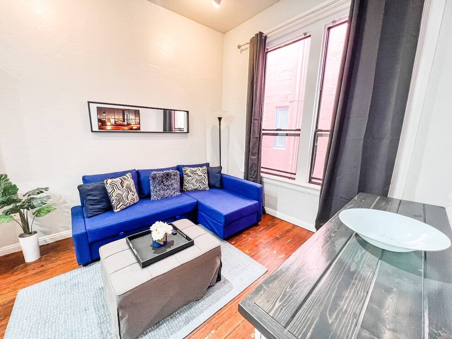 Una sala moderna con un sofá seccional azul, una mesita de centro pequeña y una mesita auxiliar de vidrio.