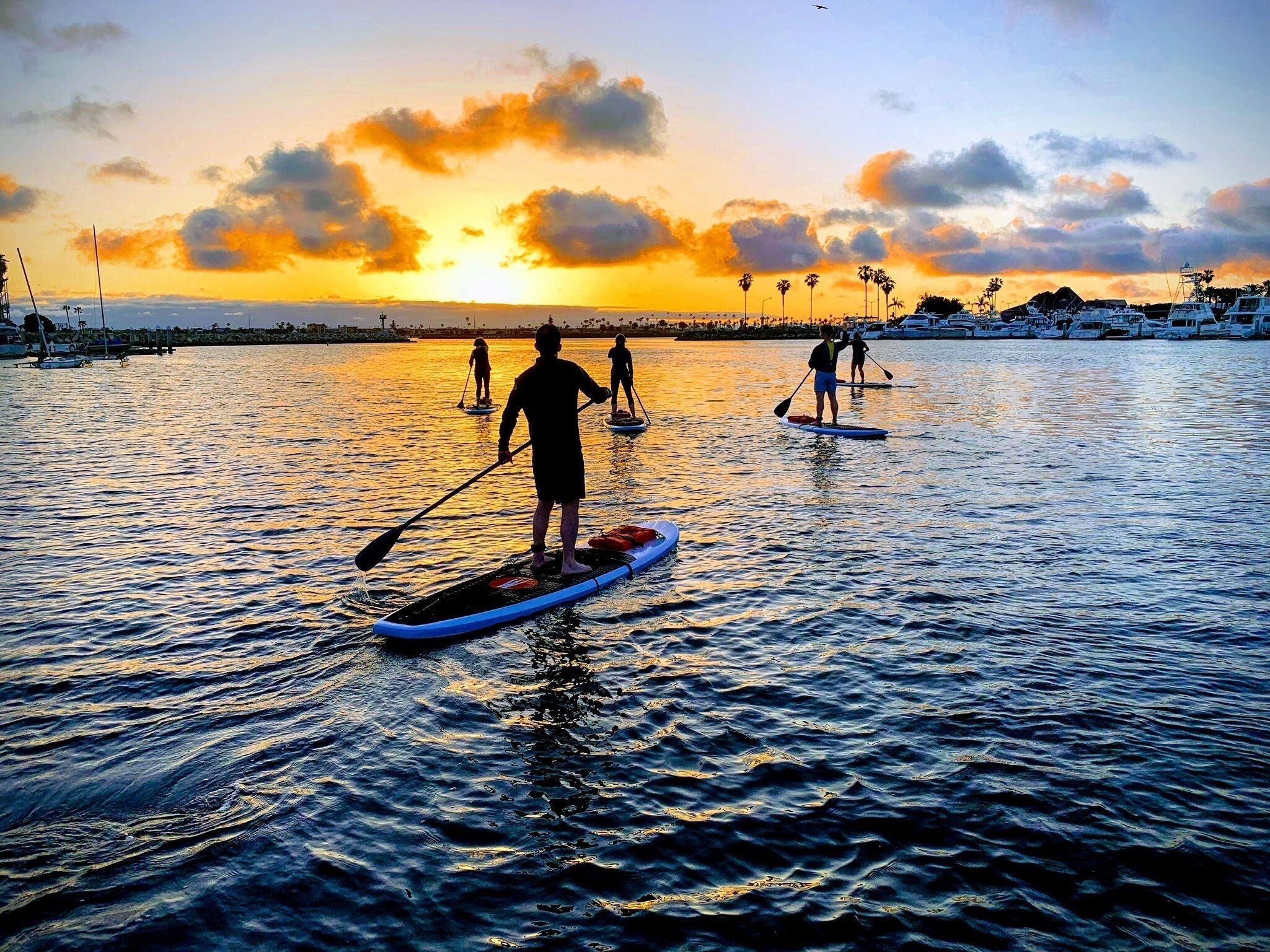 Une vue au coucher du soleil, avec des personnes pratiquant le paddle sur une étendue d’eau calme.