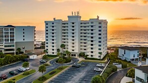 A high-rise hotel with multiple floors, a parking lot, and a view of the ocean at sunset. - Beautiful 2BR/2BA ocean view condo that feels like home (Wrightsville Beach)