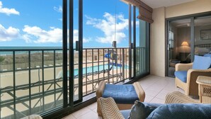 A balcony with a view of a pool and beach, wicker furniture, and a sliding glass door. - Beautiful 2BR/2BA ocean view condo that feels like home (Wrightsville Beach)