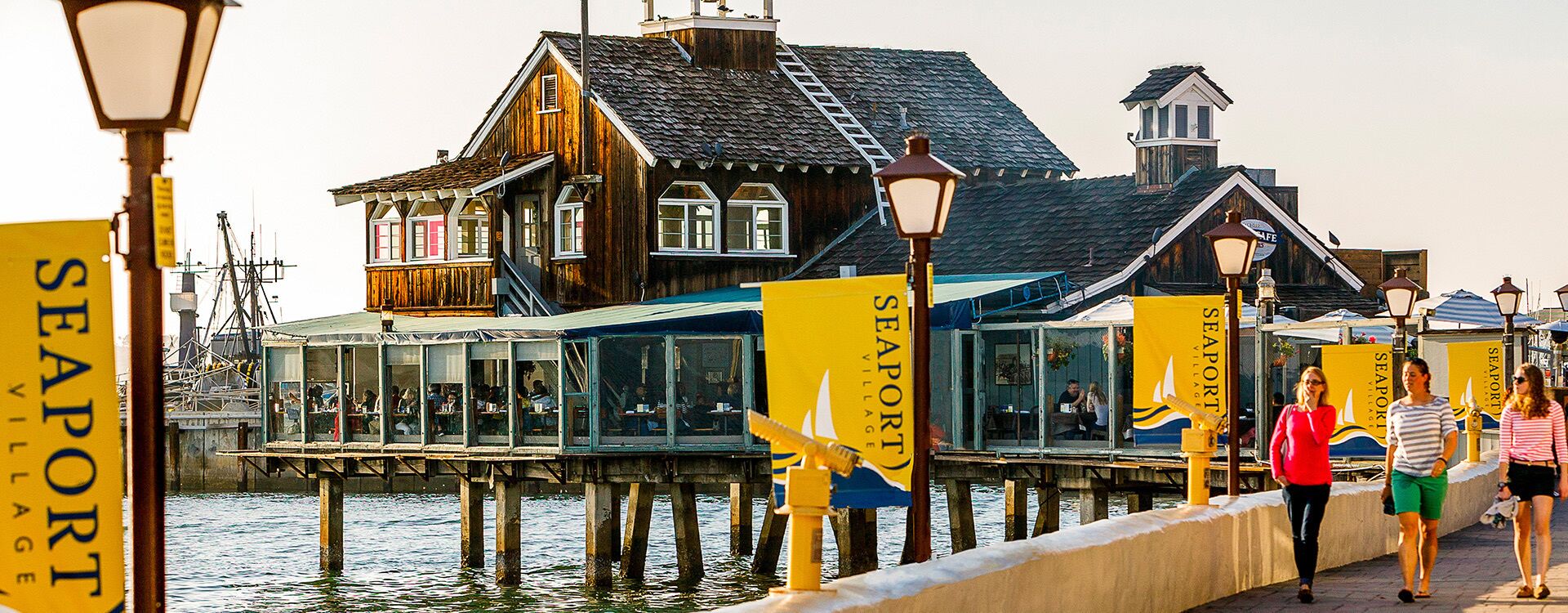 Un bâtiment en bois doté d’une jetée qui s’avance sur l’eau, comprenant un restaurant aux murs de verre et orné de banderoles jaunes.