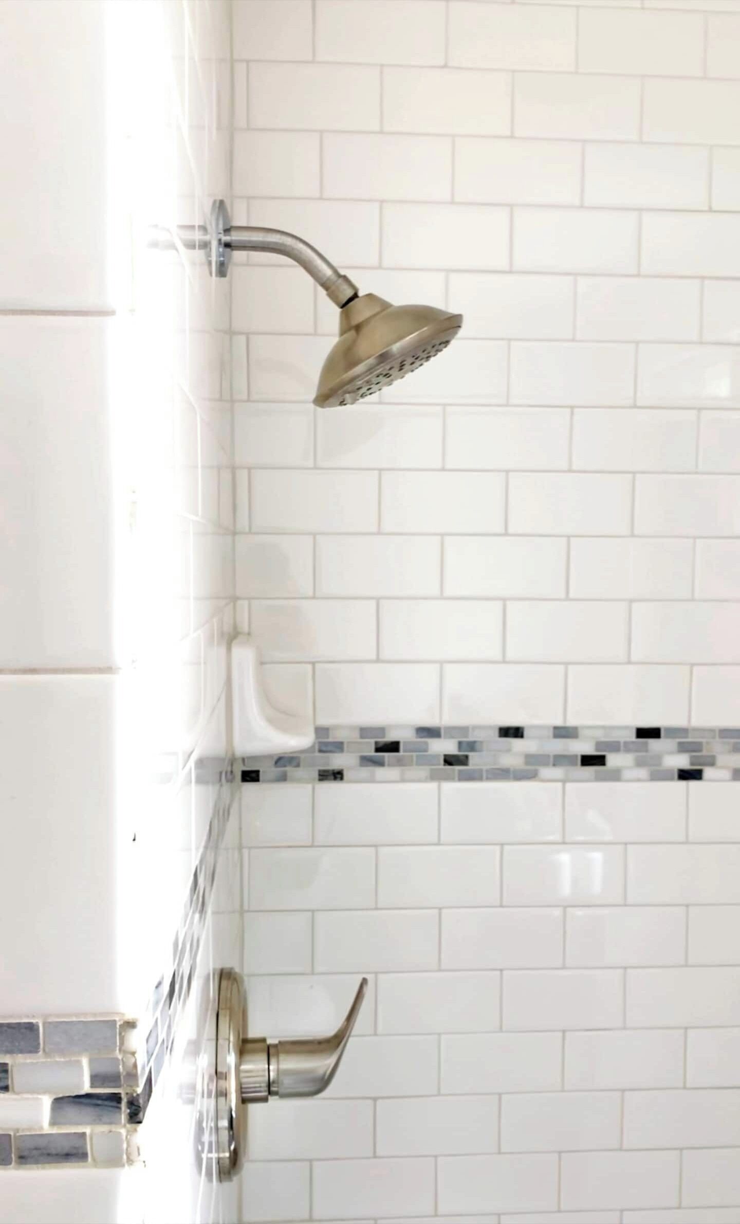 Ein Badezimmer mit weißen Fliesen im U-Bahn-Stil, einer Dusche mit gebogener Brauseleiste und einer gefliesten Rückwand mit Mosaikmuster.