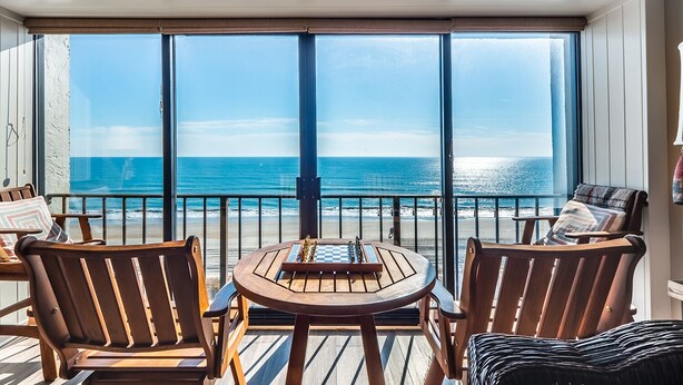 A deck with a table and chairs, overlooking a beach. - Modern 2BR/2BA condo unit w/ community pool and oceanfront view (Wrightsville Beach)