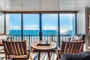 Varanda com mesa e cadeiras, com vista para uma praia.