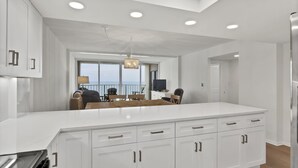 A modern kitchen with white cabinetry, a large island, and a view of the ocean. - Savor ocean views in this 2BR/2Ba condo w/community pool (Wrightsville Beach)