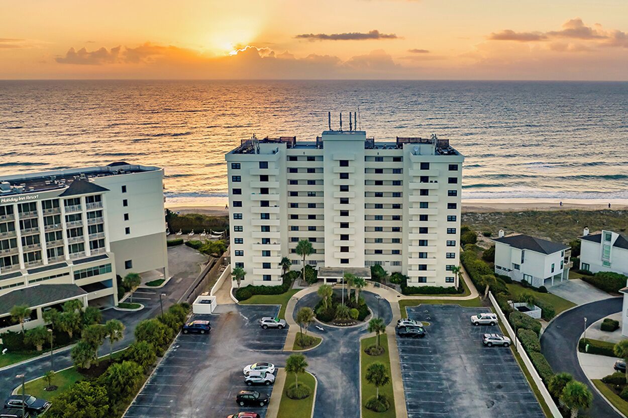 Un hotel de varios pisos con estacionamiento y vista al océano al atardecer.
