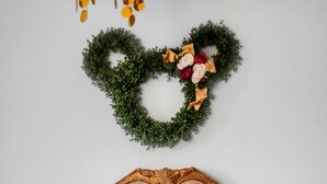 Una cama con un cabecero decorativo, ropa de cama blanca y un arreglo en forma de corazón en la pared.