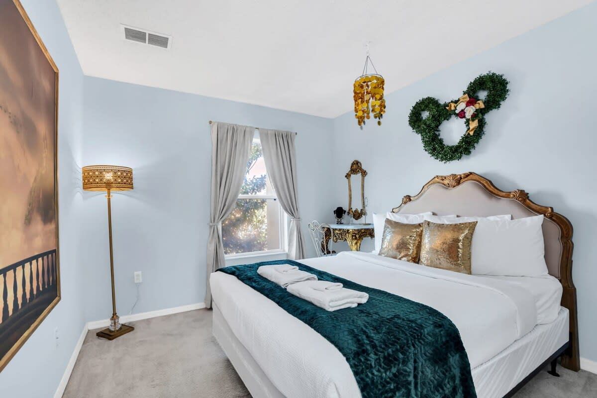 A bedroom with a bed, a nightstand, a lamp, a window with curtains, and a wall decoration.