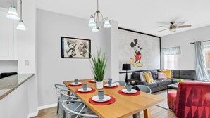 Una sala moderna con comedor, ventilador de techo y un gran mural de Mickey Mouse.