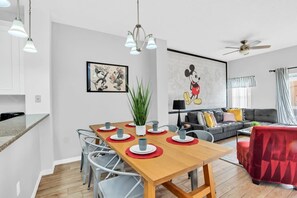 Ein modernes Wohnzimmer mit Essbereich, Deckenventilator und einer großen Wandmalerei von Mickey Mouse.