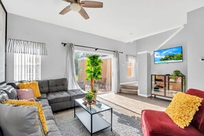 A modern living room with a grey sofa, a red armchair, a glass coffee table, and a ceiling fan.