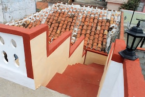 A rooftop terrace with terracotta tiles, a red and beige railing, and a black lantern. - Hostal Aniel TRINIDAD (Trinidad)