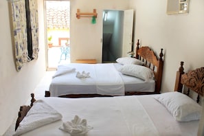 A hotel room with two beds, a wooden headboard, a small table, and a door leading to a balcony. - Hostal Aniel TRINIDAD (Trinidad)