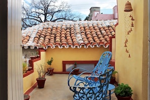 A patio with terracotta roof tiles, a blue metal chair, and potted plants. - Hostal Aniel TRINIDAD (Trinidad)