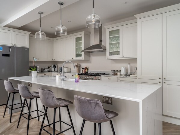 A modern kitchen with white cabinets, a large island with bar stools, stainless steel appliances, and pendant lighting.