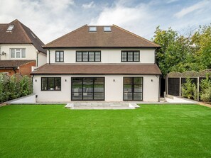 A two-story house with a large front lawn, a covered patio, and a fenced garden area.