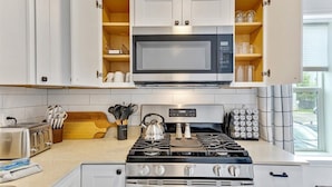 A modern kitchen with white cabinets, a stainless steel stove, a microwave, and a toaster.