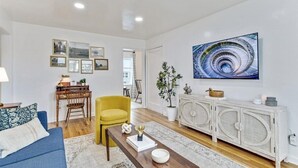 A living room with a blue sofa, yellow armchair, wooden coffee table, white cabinet, and a large abstract painting on the wall.