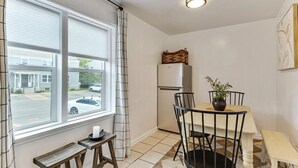 A compact kitchen with a refrigerator, a dining table with chairs, a bench, and a window with curtains.