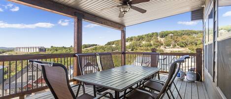 A covered outdoor deck with a table and chairs, overlooking a scenic landscape.