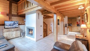 A cozy wooden cabin interior with a fireplace, a television, and a kitchen area. - Family chalet with terrace and garden in Chamonix (Chamonix-Mont-Blanc)