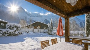 A snow-covered outdoor dining area with a table and chairs, a wooden ceiling, and a view of snow-covered mountains. - Family chalet with terrace and garden in Chamonix (Chamonix-Mont-Blanc)