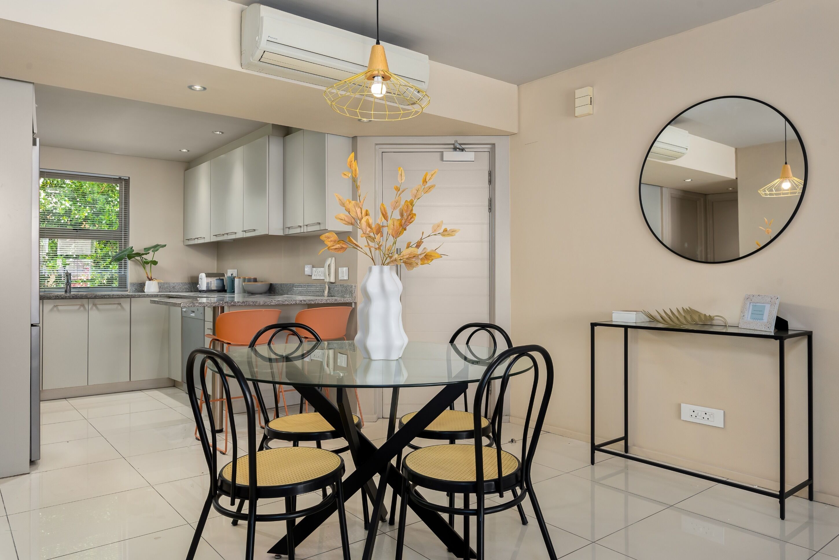 A modern kitchen with white cabinets, a dining table with four chairs, and a vase with dried flowers.