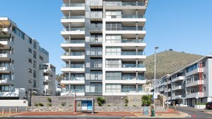 A multi-story residential building with balconies, a bus stop, and a stone wall with plants. - Luxe 2-Bed in Trendy Green Point , Pool Views (Cape Town)