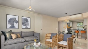 A modern living room with a grey sofa, wicker chairs, a glass coffee table, and artwork on the wall. - Luxe 2-Bed in Trendy Green Point , Pool Views (Cape Town)