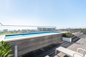 Una piscina sul tetto con vista sulla città, un pontile in legno e un’area salotto all'aperto.