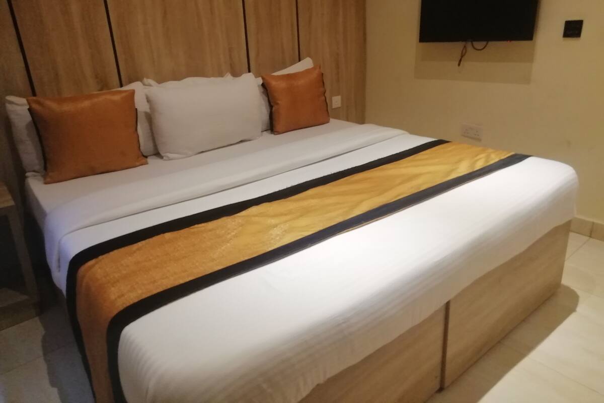 A neatly made bed with a white and black striped blanket, a wooden headboard, and a television mounted on the wall.