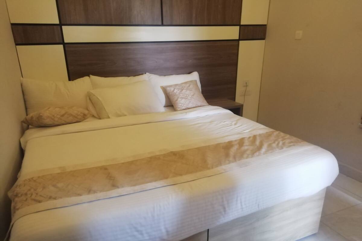 A neatly made bed with a patterned bedspread and pillows, a wooden headboard, and a bedside table with a lamp.