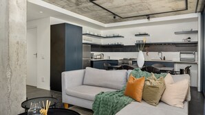 Ein modernes Wohnzimmer mit grauem Sofa, einem Couchtisch und einem Essbereich, im Hintergrund ist eine Küche zu sehen.