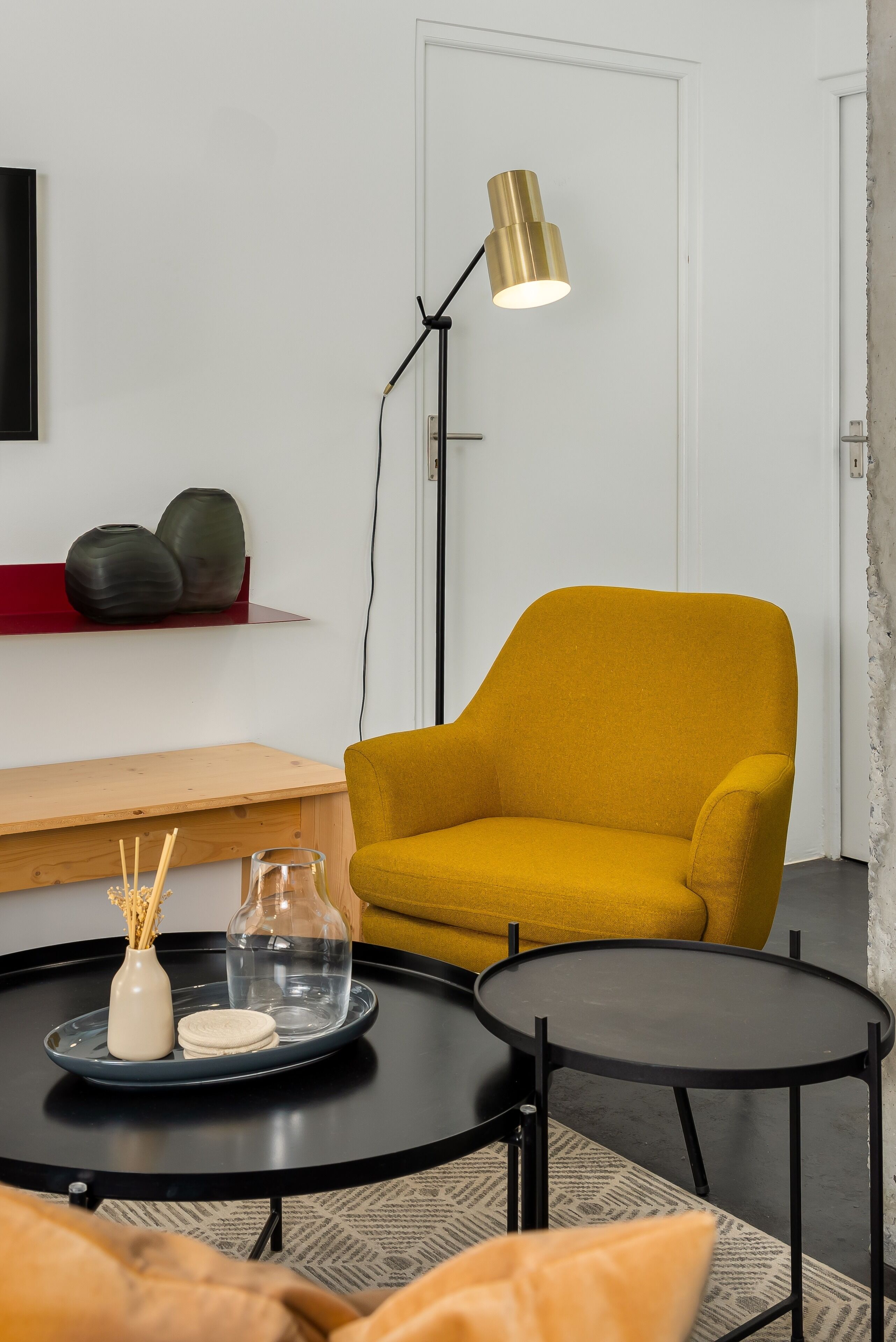 A modern living room with a mustard-colored armchair, a black floor lamp, a round coffee table, and a small side table with decorative items.