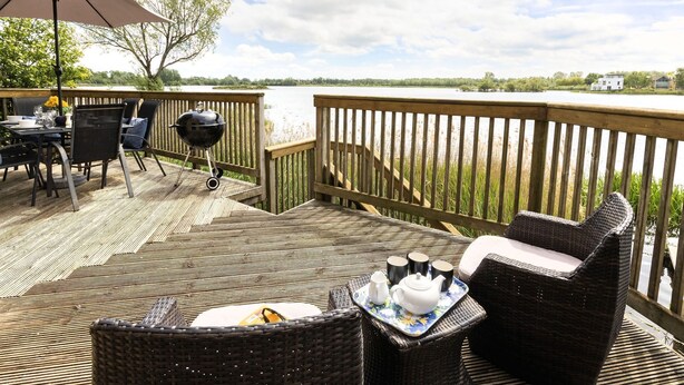 Eine Terrasse mit Gartenmöbeln, einem Grill und Blick auf einen See.