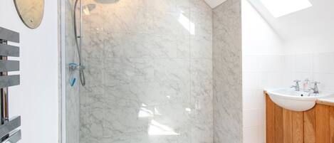 Een moderne badkamer met een douchecabine van glas, marmeren tegels, een dakraam en een houten wastafelmeubel met een wastafel.
