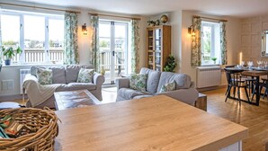 Uma sala de estar moderna com uma mesa de centro de madeira, dois sofás, uma mesa de jantar com cadeiras e uma grande janela com cortinas.