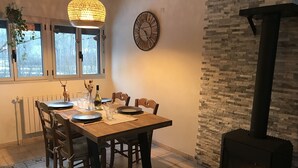 A dining area with a wooden table set for four, a large wall clock, and a stone fireplace. - Bourg d'Oisans, a cyclist's paradise (Le Bourg-d'Oisans)