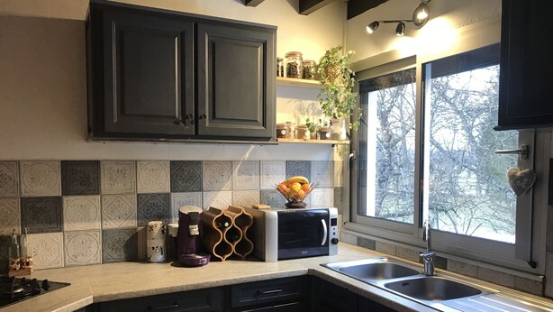 A kitchen with dark cabinets, a built-in oven, a microwave, and a sink. There are decorative tiles on the backsplash and a window with a view of trees. - Bourg d'Oisans, a cyclist's paradise (Le Bourg-d'Oisans)