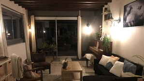 A cozy living room with a black sofa, a wooden coffee table, and a piano. There is a sliding glass door leading to a balcony with plants. - Bourg d'Oisans, a cyclist's paradise (Le Bourg-d'Oisans)