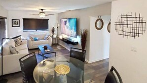 Ein modernes Wohnzimmer mit einem Glastisch, schwarzen Stühlen, einer Couch und einem Deckenventilator.