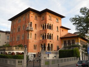 A multi-story building with a symmetrical facade, arched windows, and a balcony on the second floor. - STUDIO APARTMENT WITH A SMALL GARDEN (Lido)