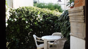 A patio with a white table and chairs, a metal grill, and a tiled floor. - STUDIO APARTMENT WITH SMALL GARDEN (Lido)