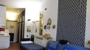 A compact room with two single beds, a small desk, a mirror, and a patterned curtain. - STUDIO APARTMENT WITH SMALL GARDEN (Lido)