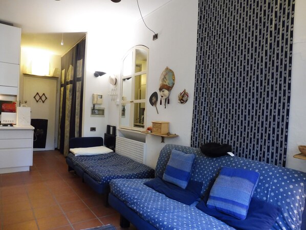 A compact room with two single beds, a small desk, a mirror, and a patterned curtain. - STUDIO APARTMENT WITH A SMALL GARDEN (Lido)