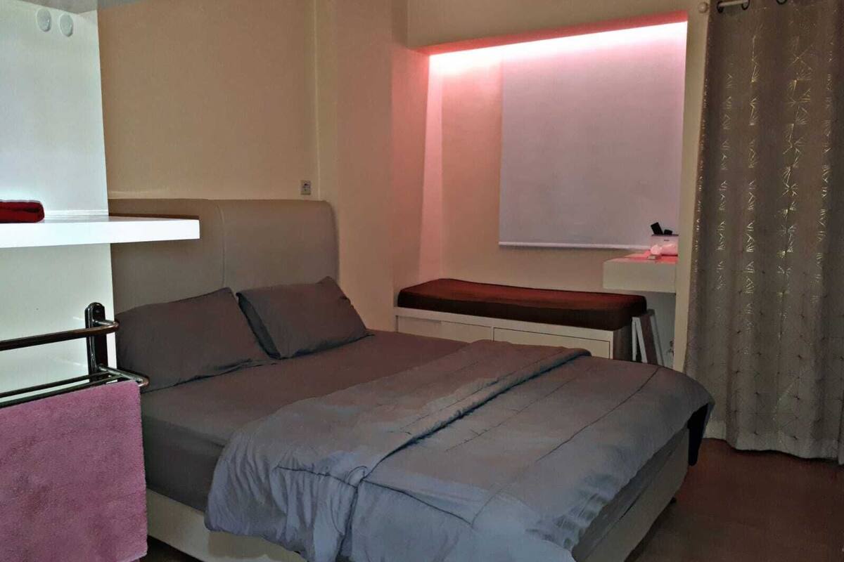 Ein Schlafzimmer mit Bett, Nachttisch, einem Fenster mit Vorhängen und einem Wandregal.