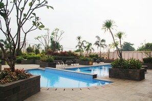 Ein rechteckiger Pool mit Fliesenrand, umgeben von Pflanzkästen mit verschiedenen Pflanzen und Bäumen, sowie Gartenmöbeln.