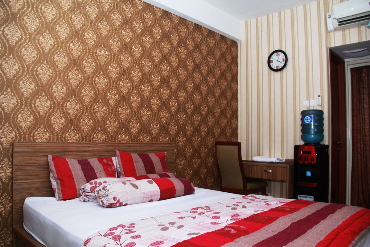 Ein Hotelzimmer mit Bett, Schreibtisch, Stuhl, Wasserspender und einer Wanduhr.