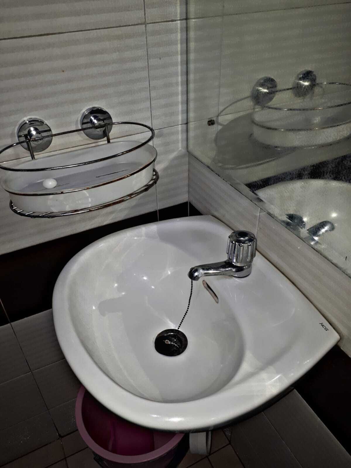 A bathroom with a white sink, a chrome faucet, a glass soap dish, and a mirror above the sink.