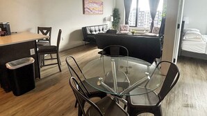 A modern living room with a glass-top dining table, black chairs, a sofa, and a large window with curtains.